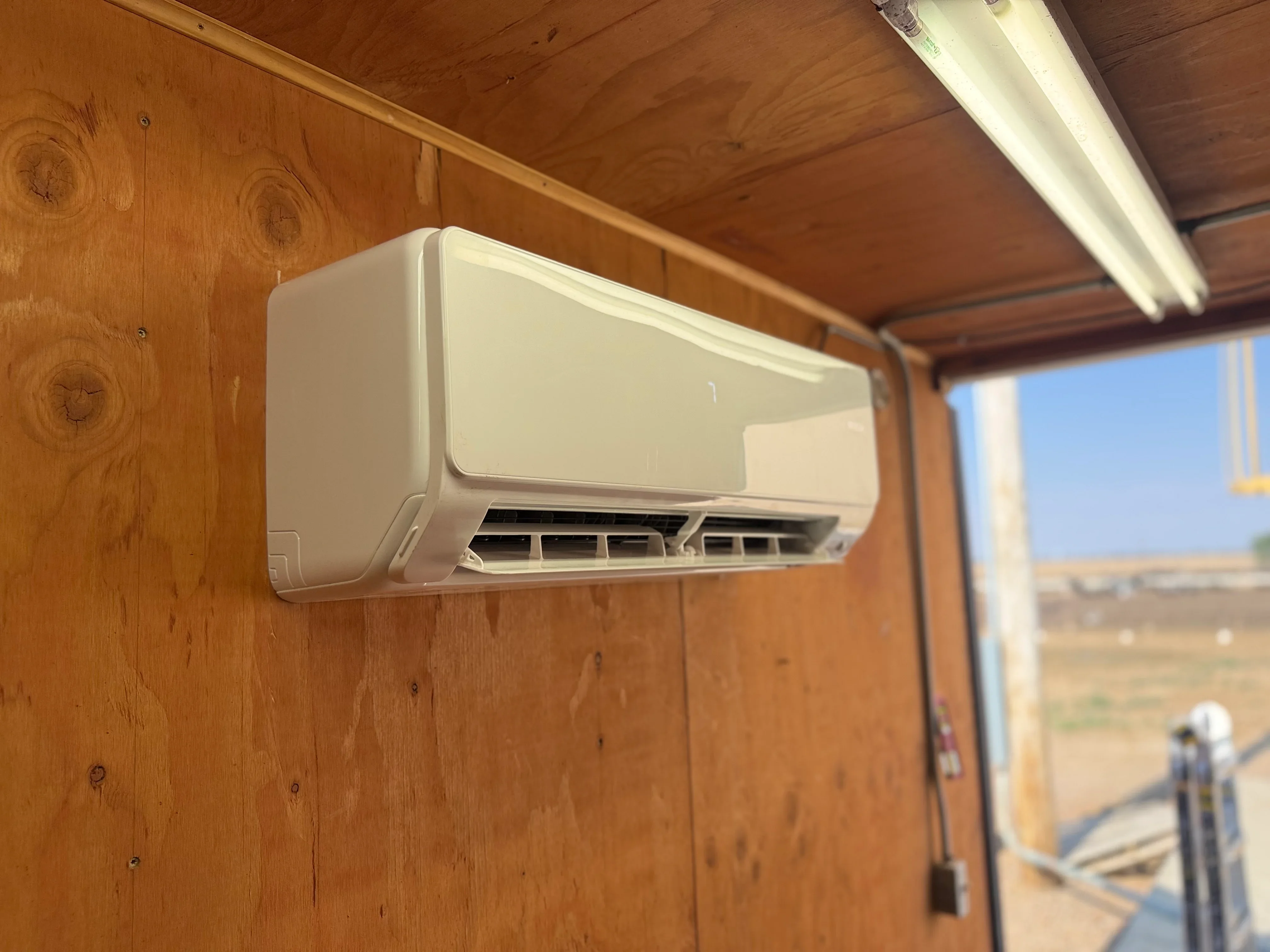 White mini-split AC unit mounted on wooden wall with clear sky visible through window