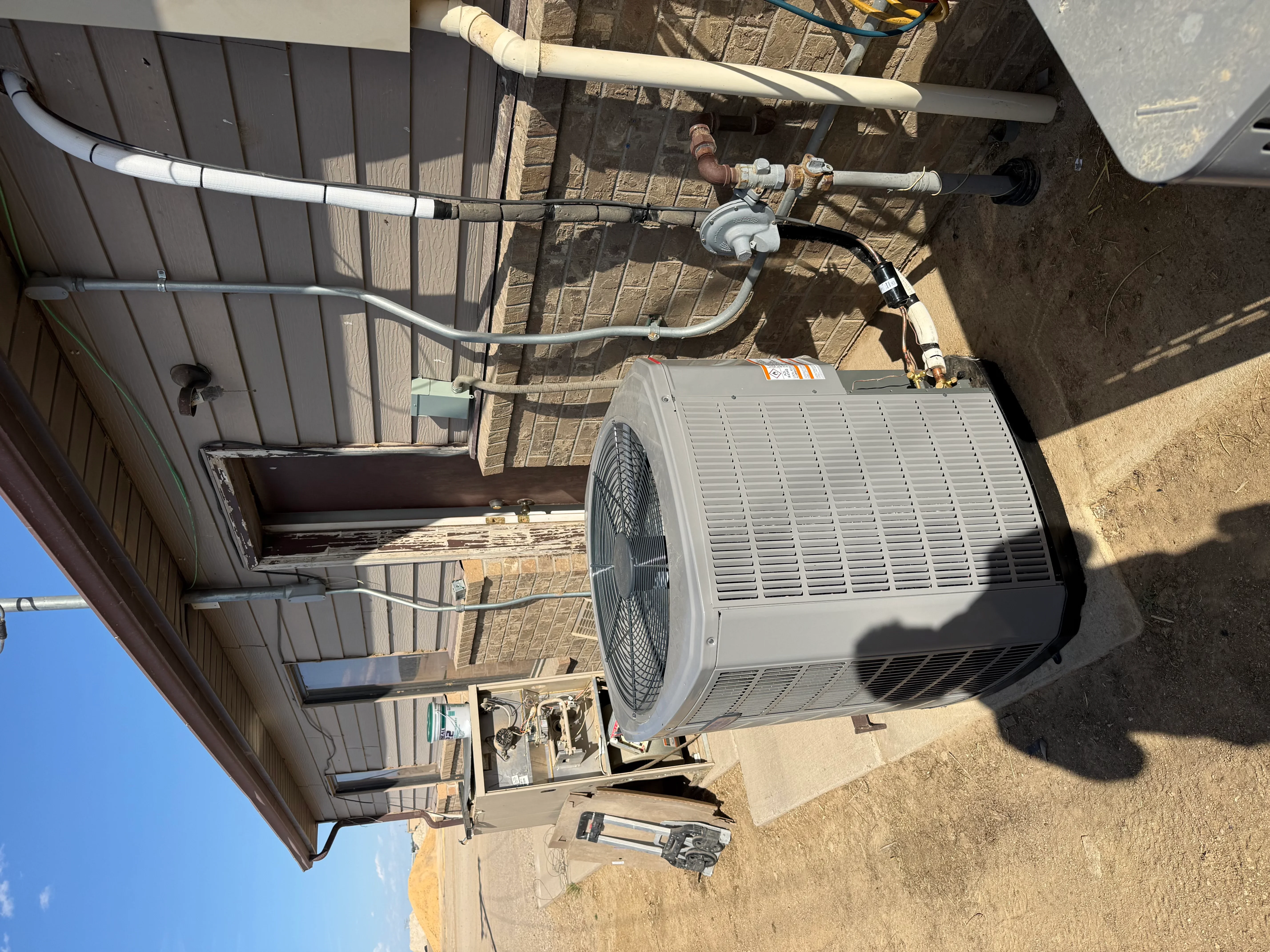 Newly installed residential AC condenser unit with refrigerant lines and drainage system