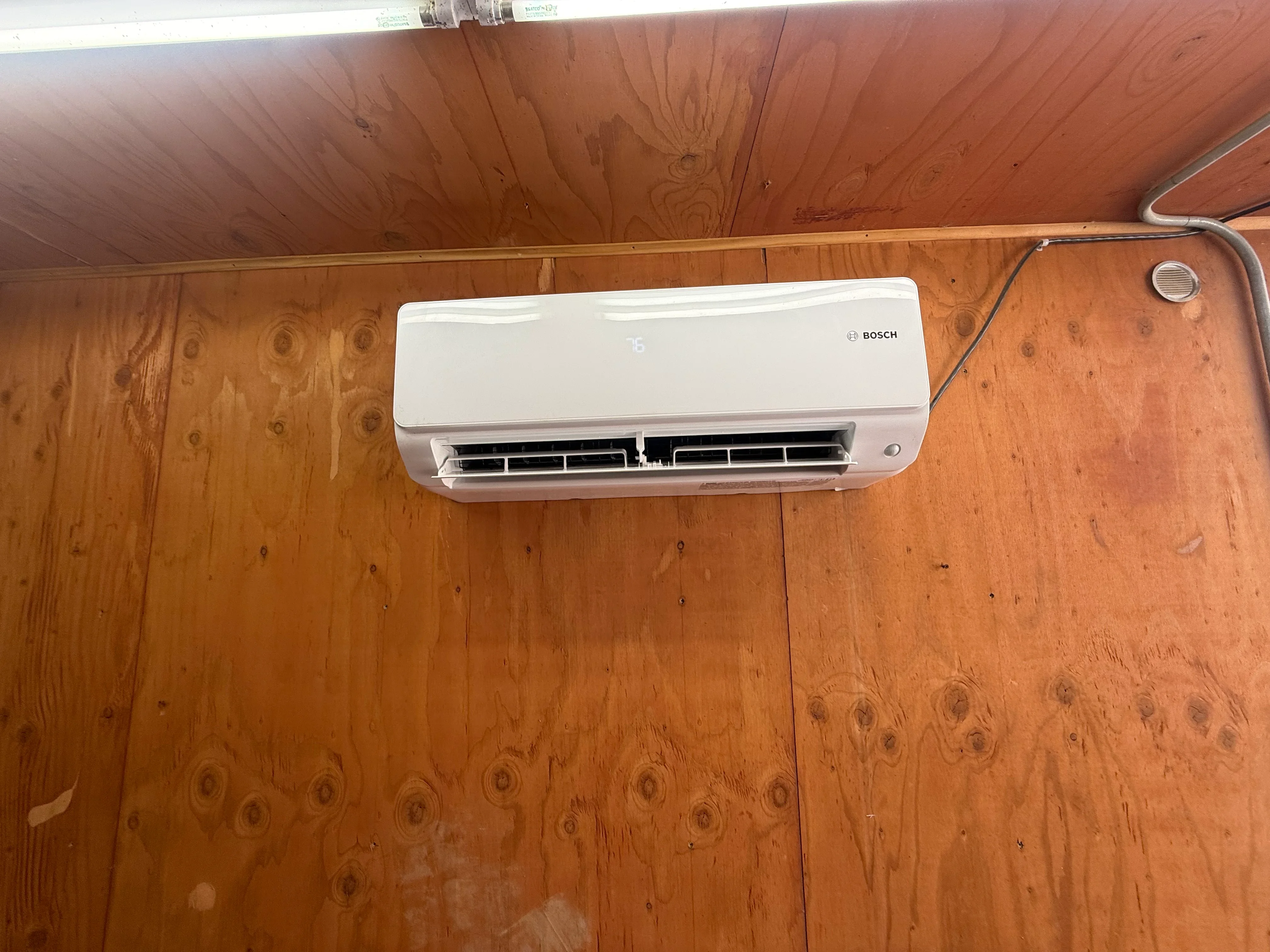 White Bosch mini-split AC unit mounted on wood wall with refrigerant lines