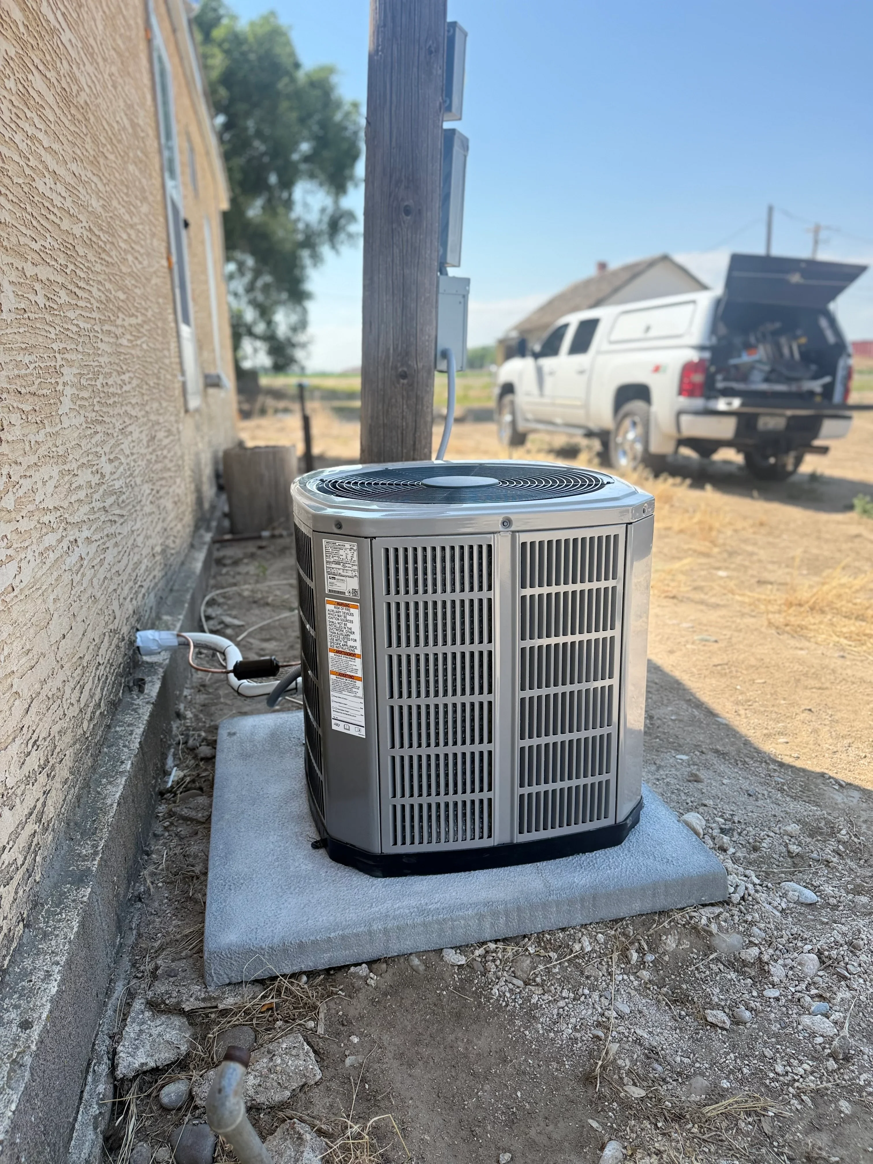New AC condenser unit installed on concrete pad next to brick home exterior