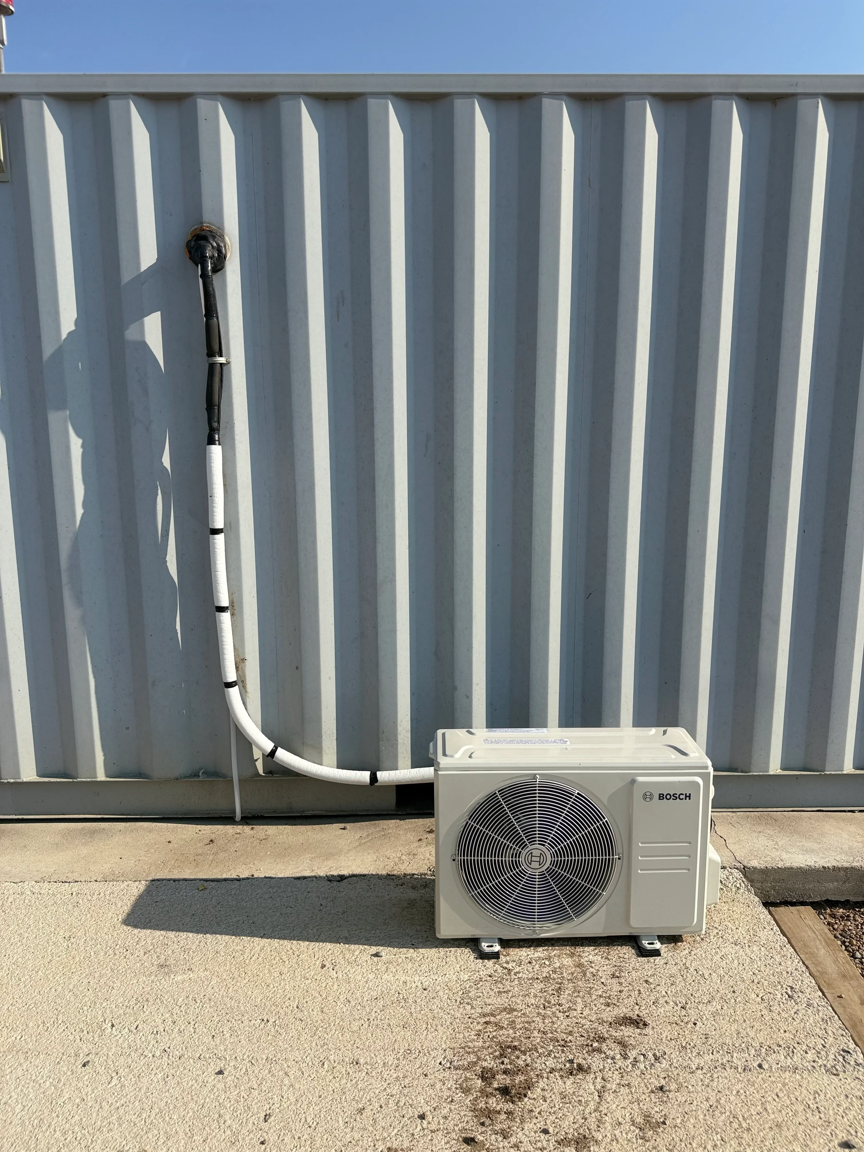 Bosch ductless mini-split outdoor condenser unit with white refrigerant lines against corrugated metal wall