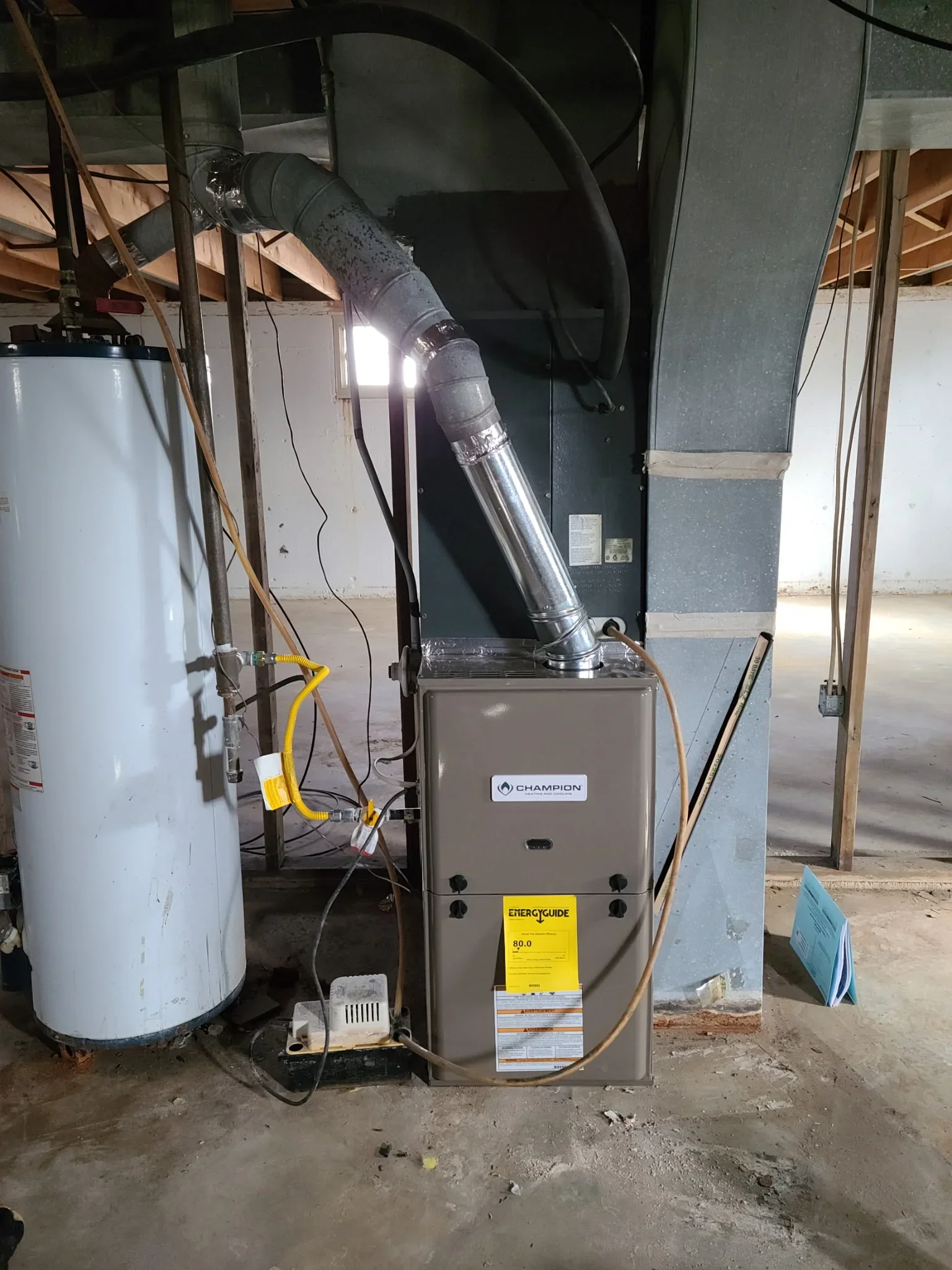 Champion furnace installation with metal ductwork, water heater, and yellow Energy Guide label