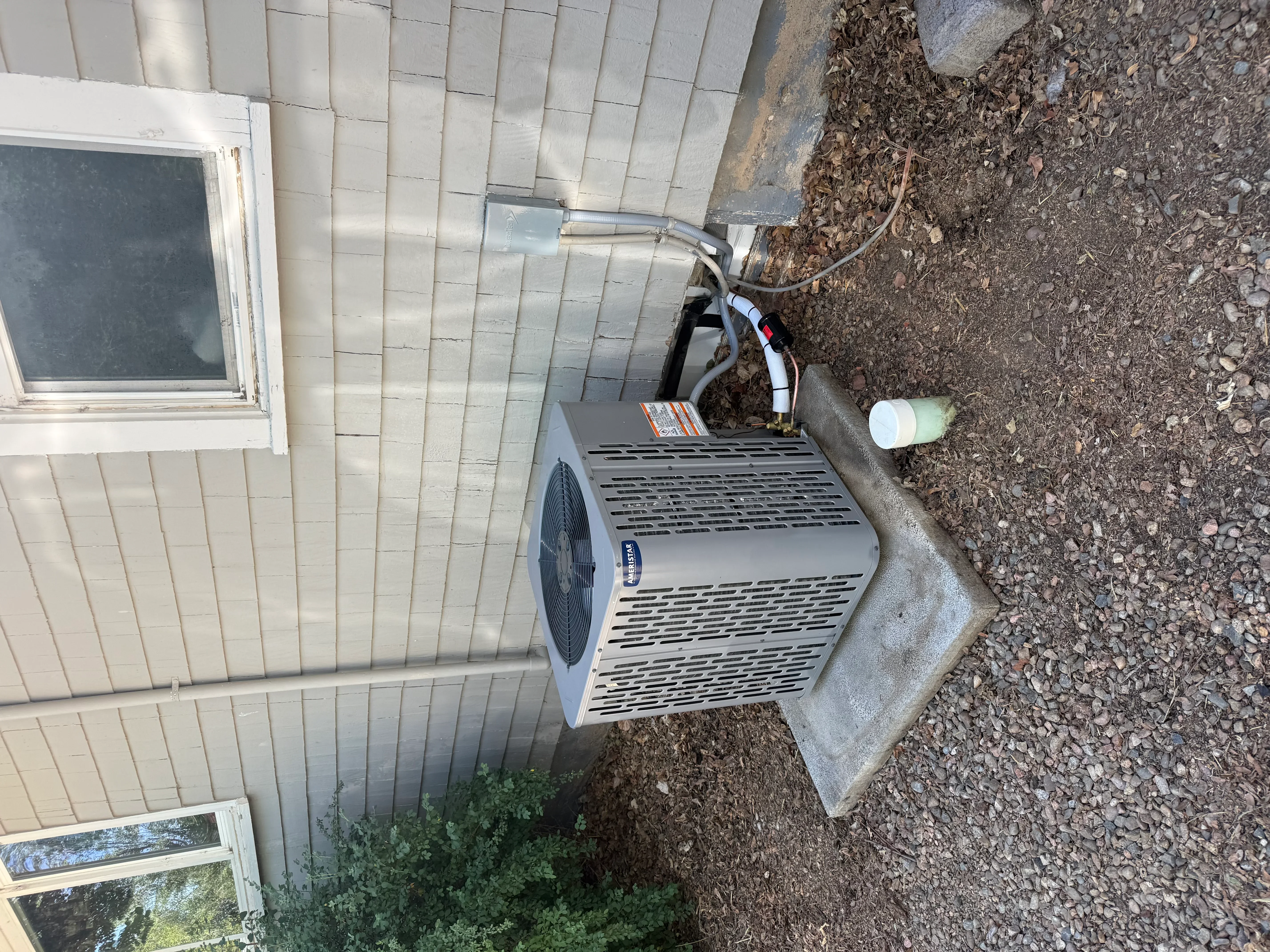 Outdoor AC condenser unit installed on concrete pad with refrigerant lines and electrical connections