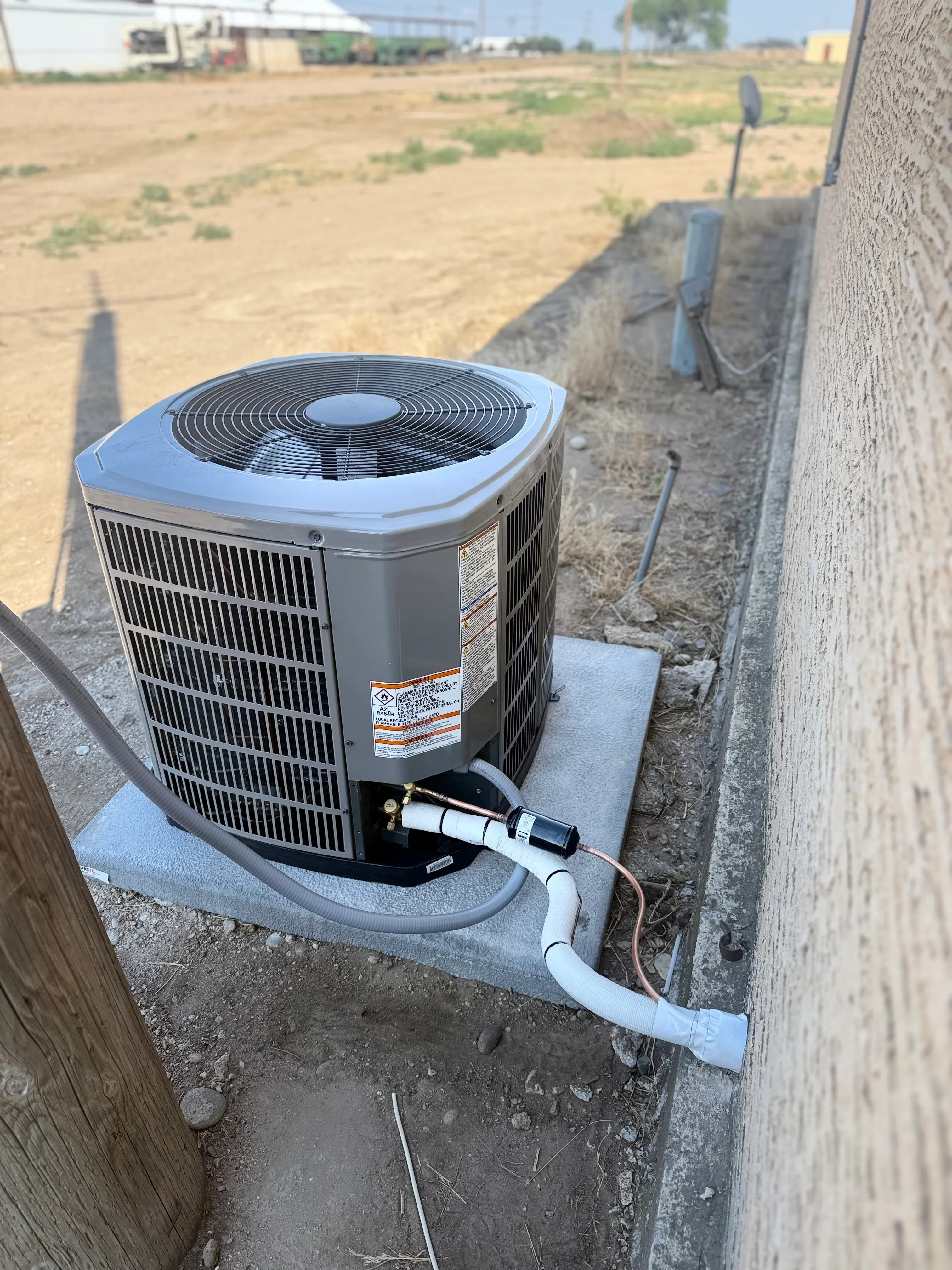 New AC condenser unit installed on concrete pad with white PVC piping connections