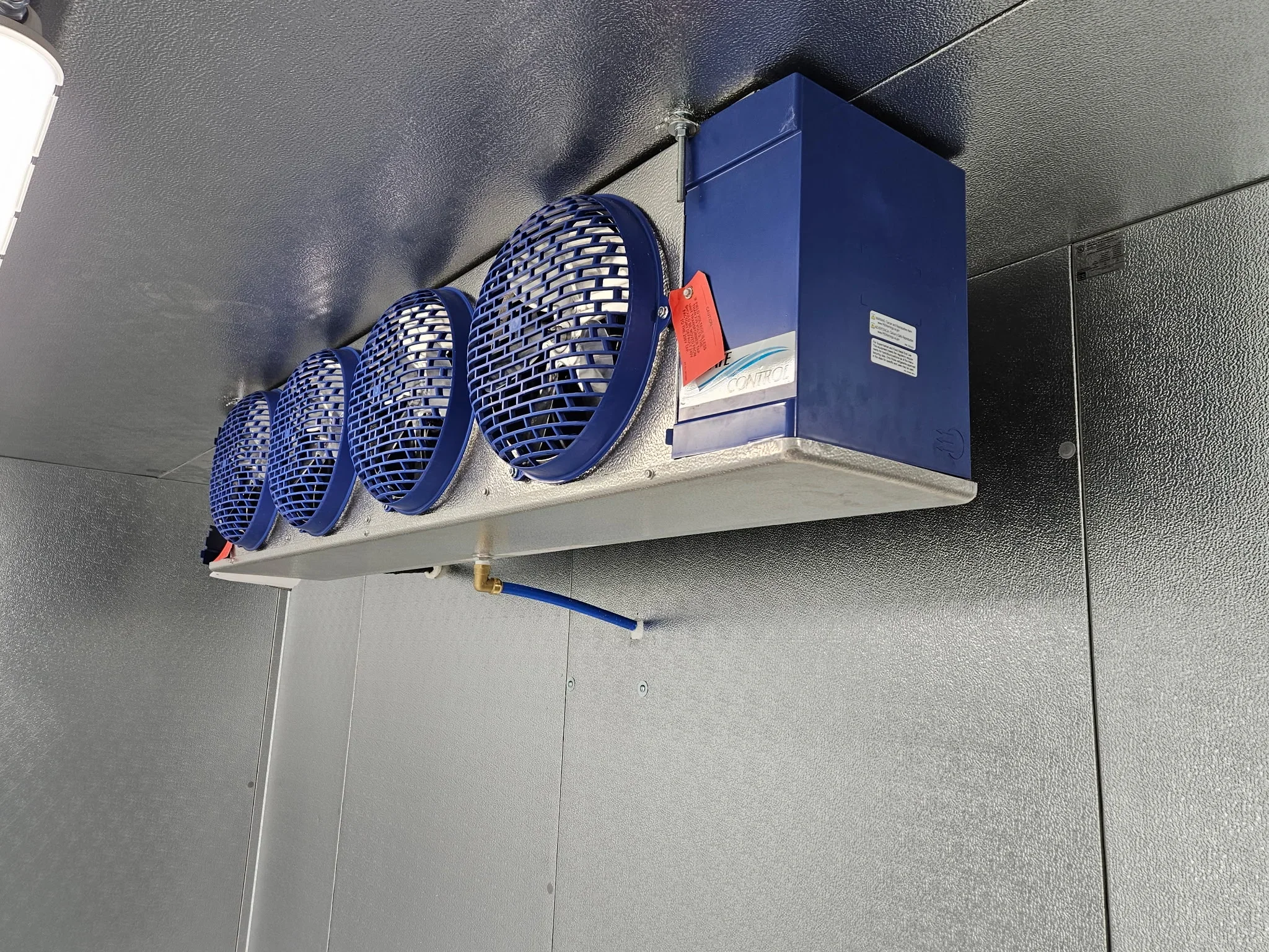 Commercial evaporative cooler with three blue fans mounted on interior wall
