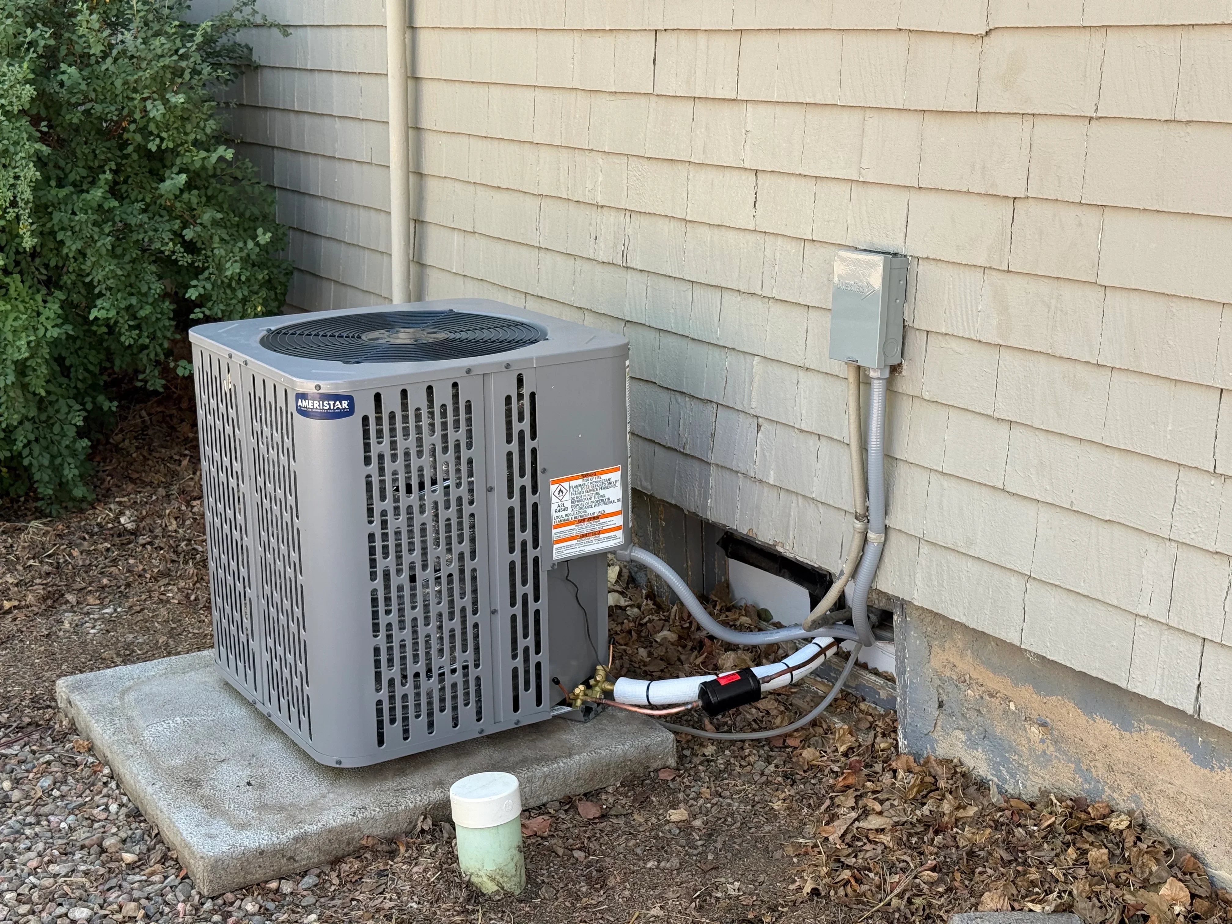 Gray HVAC condenser unit installed on concrete pad with refrigerant lines and disconnect switch