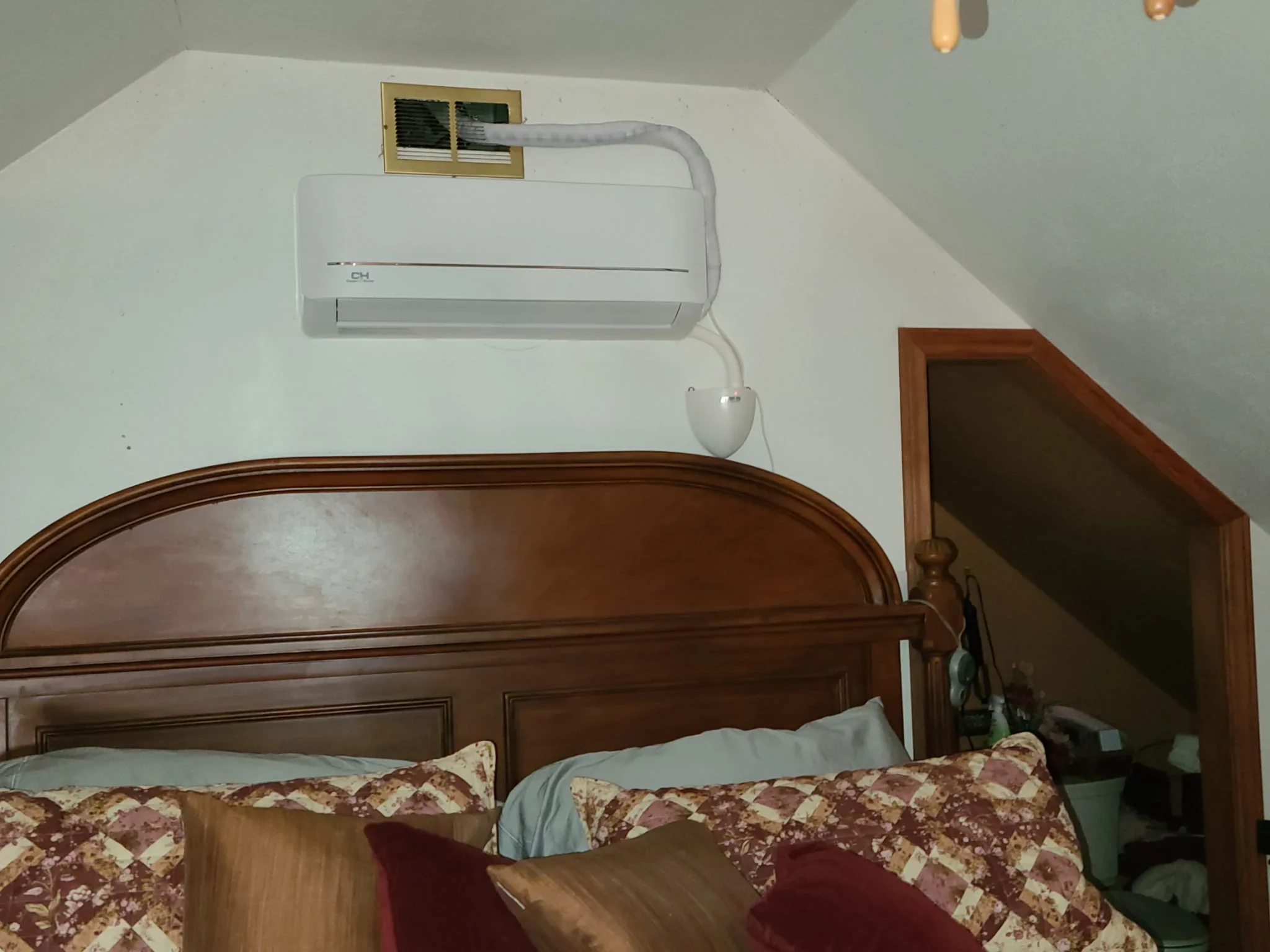 White ductless mini-split AC unit mounted on bedroom wall above wooden bed