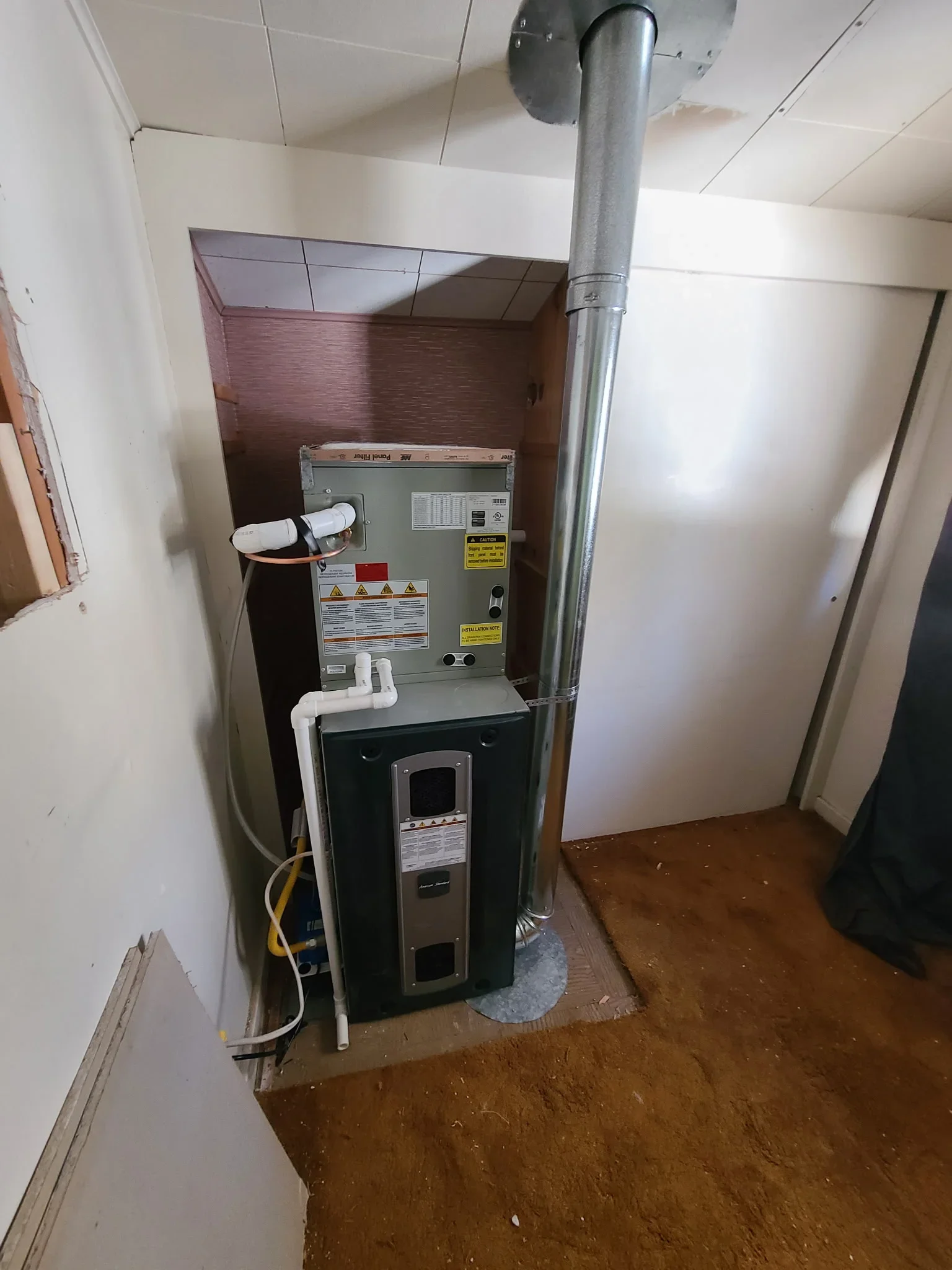 Newly installed furnace with ductwork and metal exhaust pipe in basement utility closet