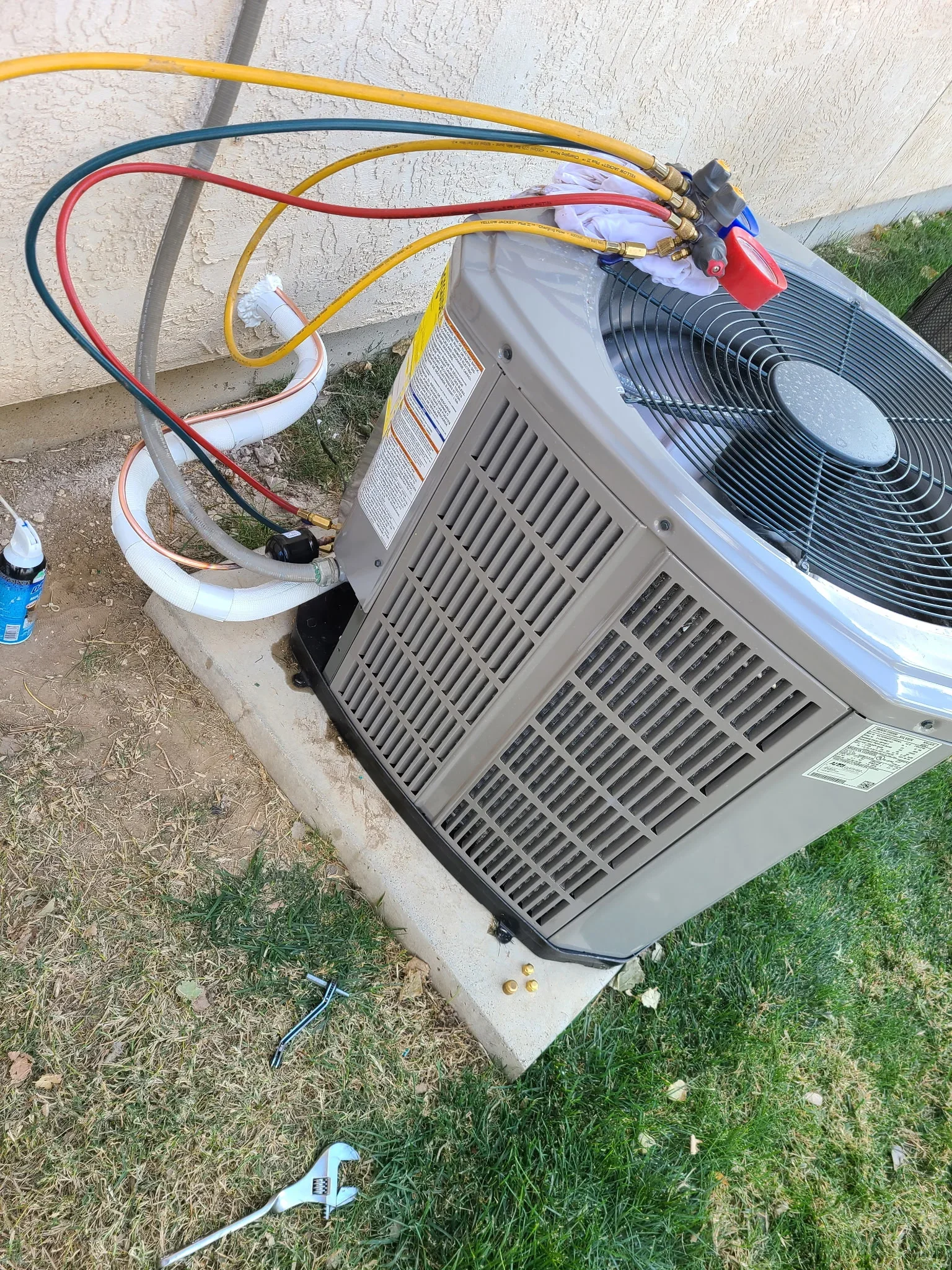 Installed AC condenser unit with color-coded refrigerant lines on concrete pad