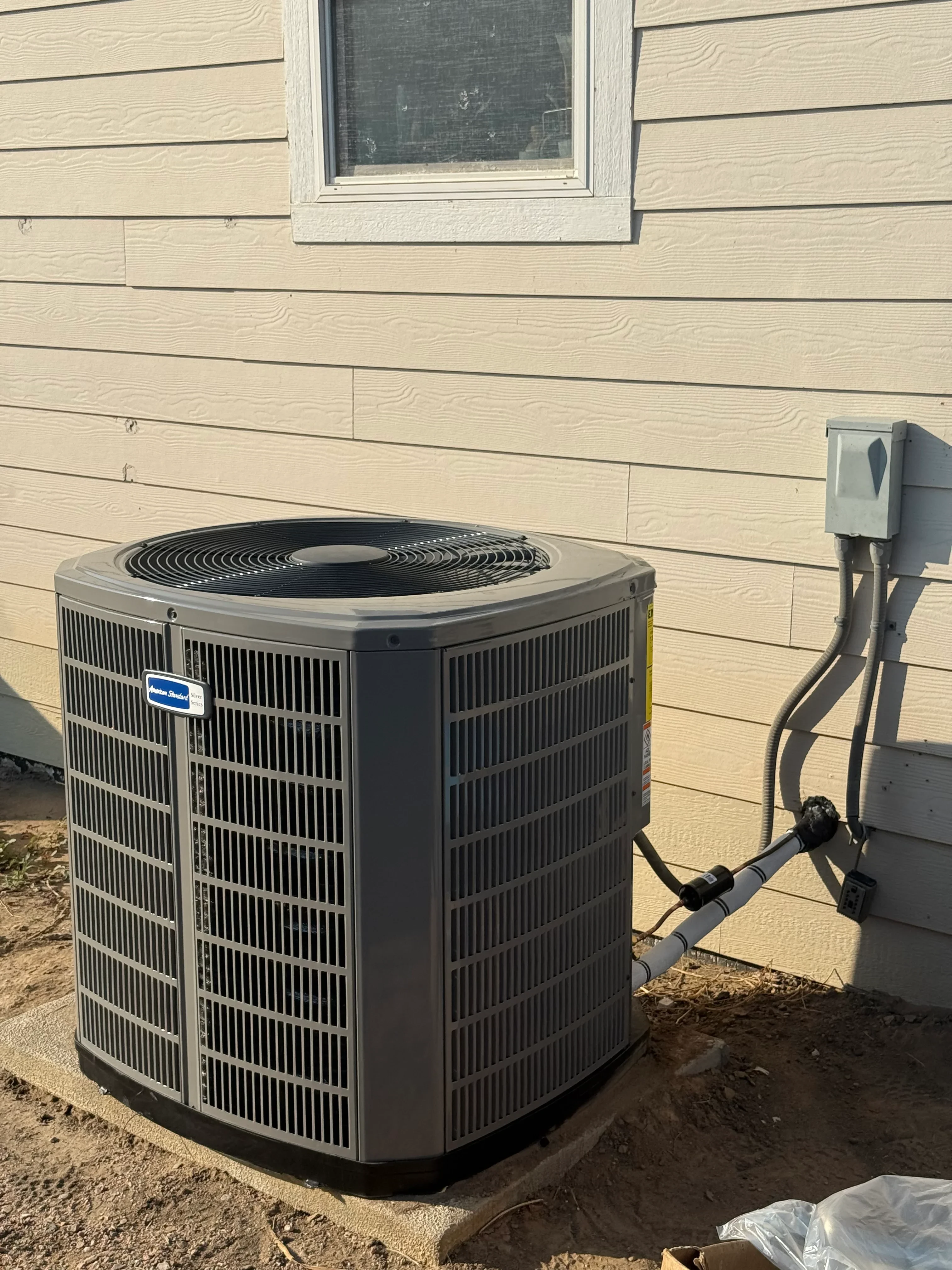 Installed AC condenser unit on concrete pad next to wood-sided house