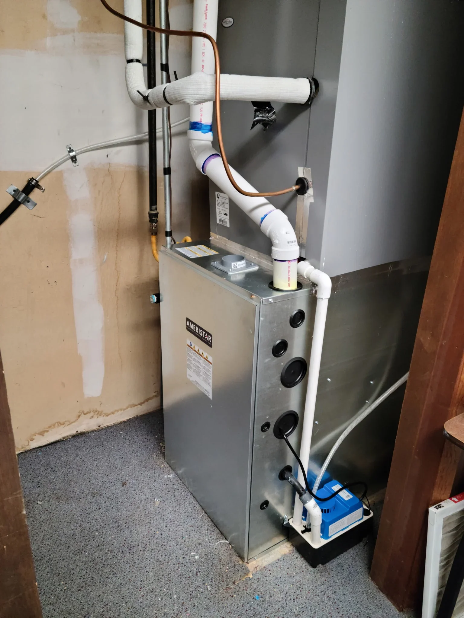 Newly installed Ameristar furnace with white PVC ductwork and copper refrigerant lines in basement